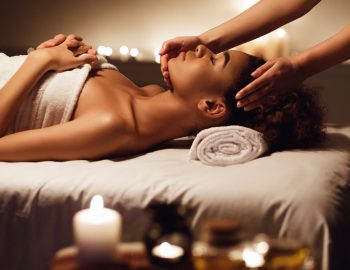 African girl having face massage, relaxing in spa salon, side view